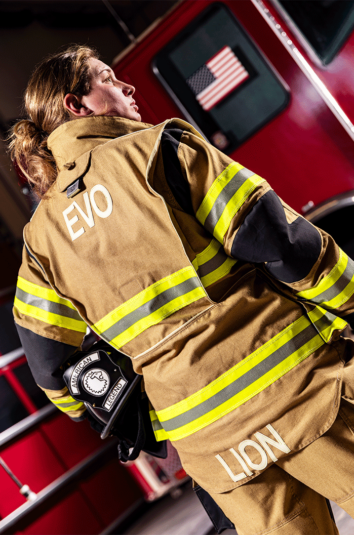 Rear view of a firefighter wearing LION V-Force EVO turnout gear beside a fire engine