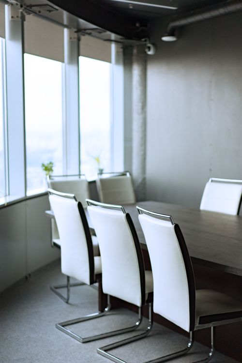 Empty corporate boardroom with a conference table, white chairs, and floor-to-ceiling windows